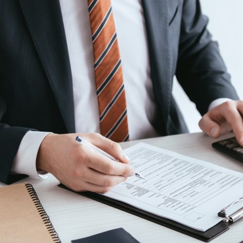 cropped view of man counting on calculator while holding pen near document  isolated on white